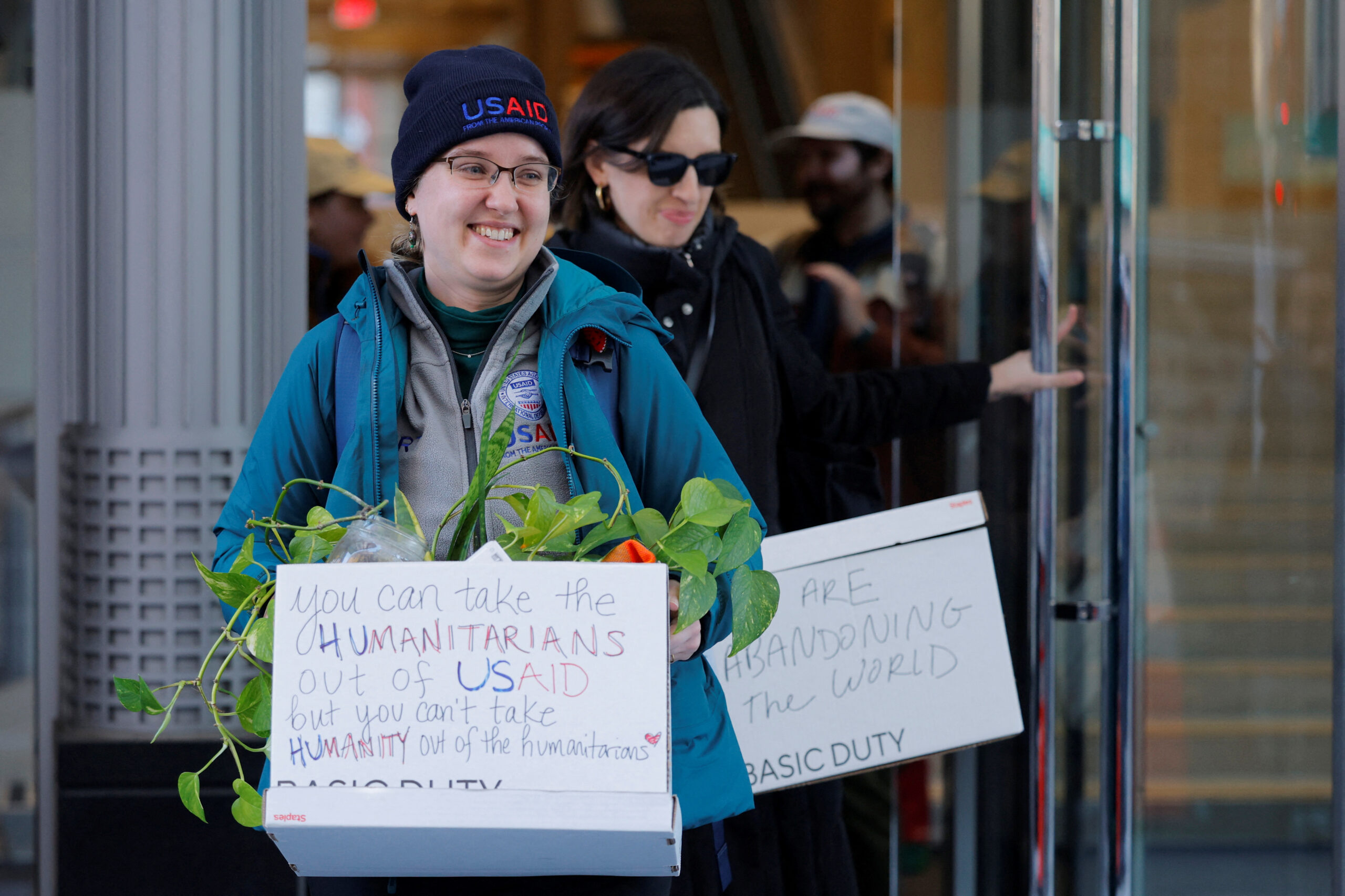 Axed USAID employees smile as they haul personal belongings — with messages for Trump — out of DC office 